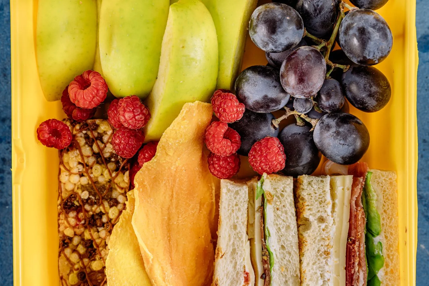 An open lunch box with fruit and a sandwich.